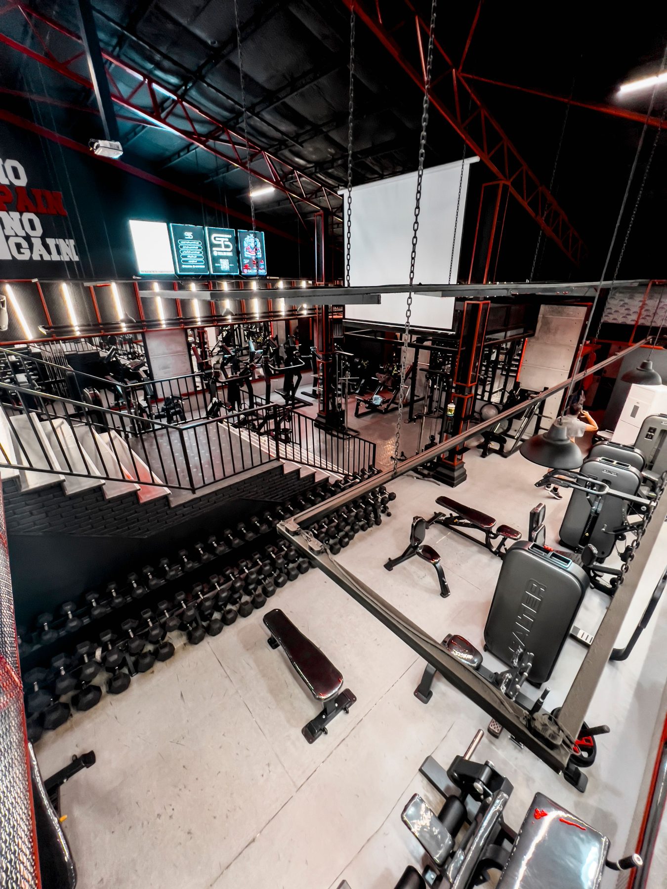 The gym floor seen from above, with red steel beams and racks of dumbbells