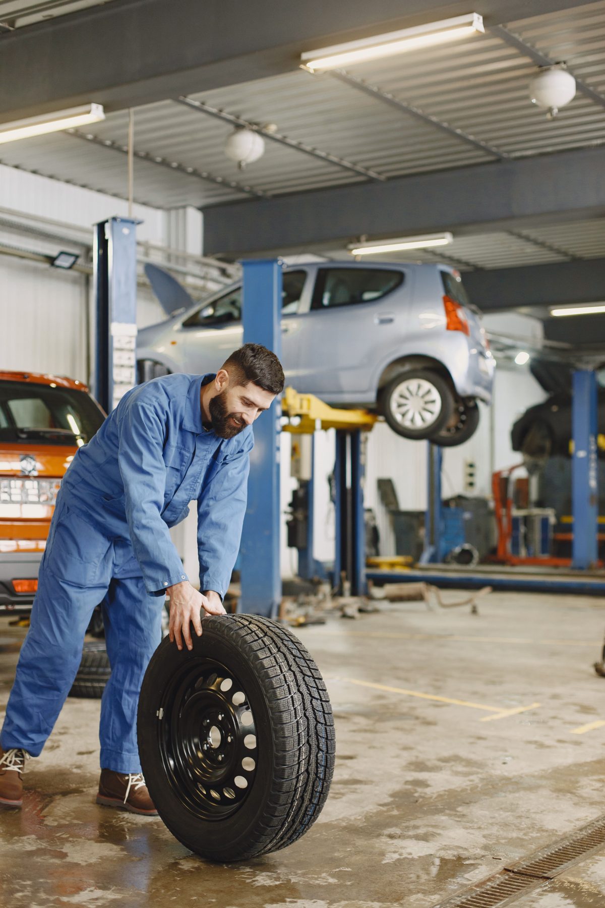 A smiling mechanic rolling a tyre across a garage floor