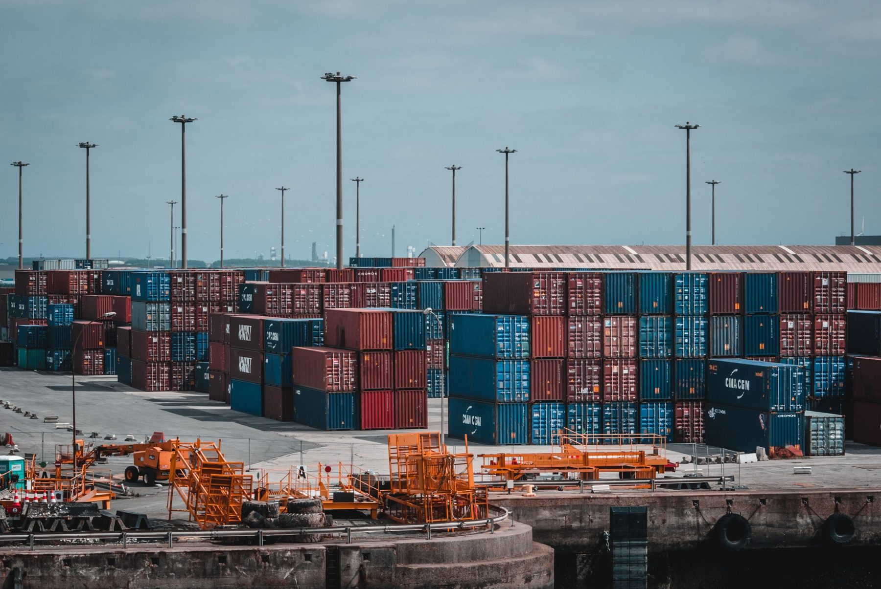 A container port yard with stacked containers and orange cranes