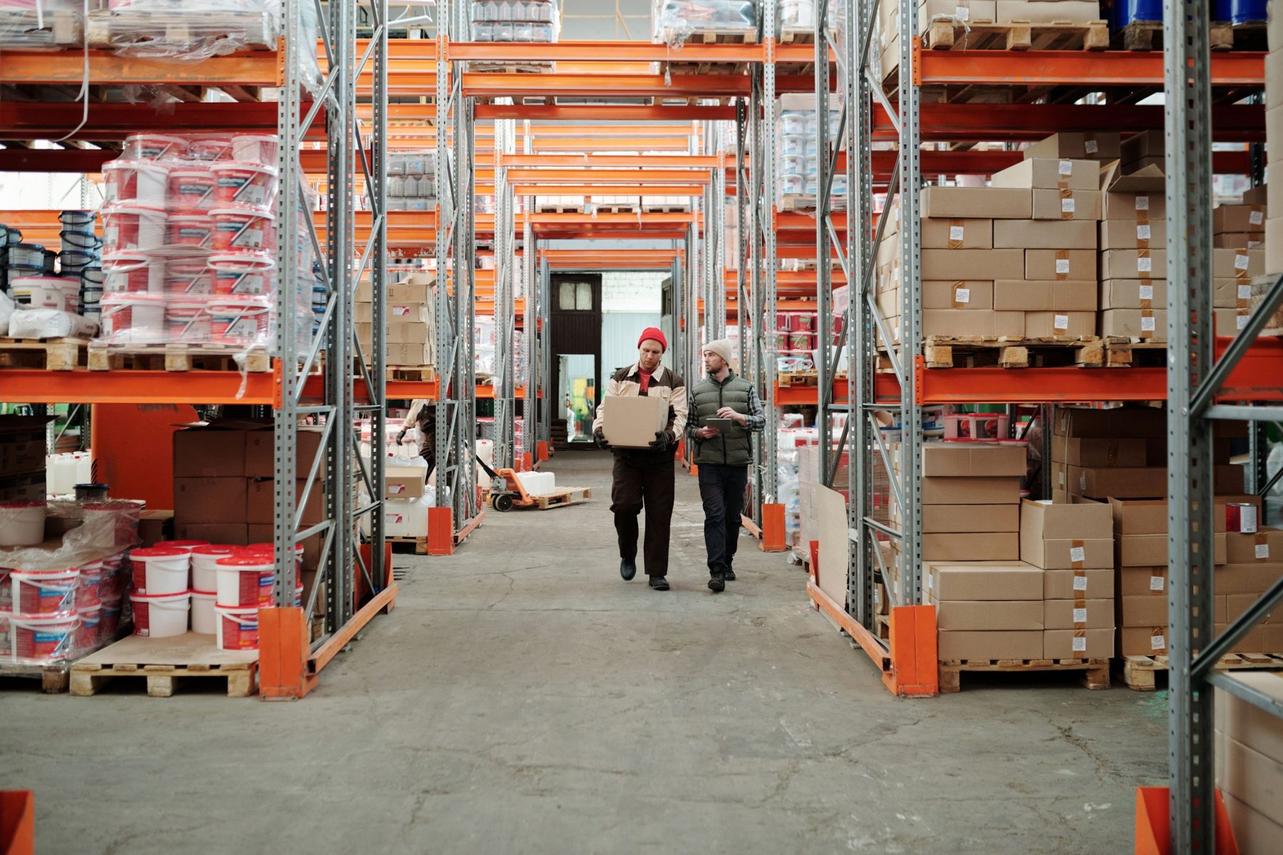 Two warehouse staff walking down an aisle with orange racking