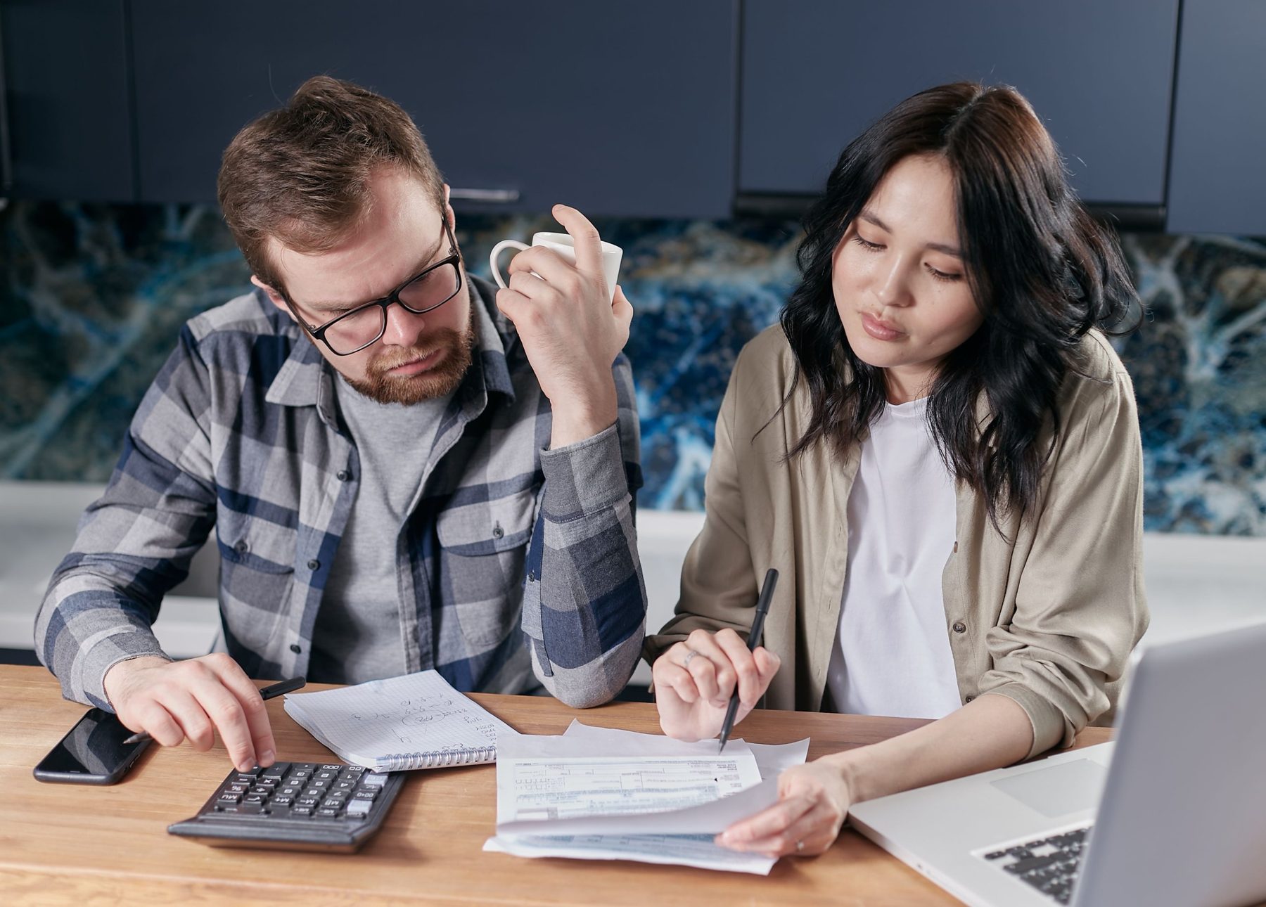 A couple at their kitchen table working through mortgage forms with a calculator